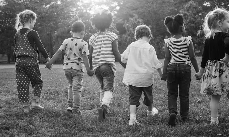 Black and white photograph of group of children holding hands walking away from camera