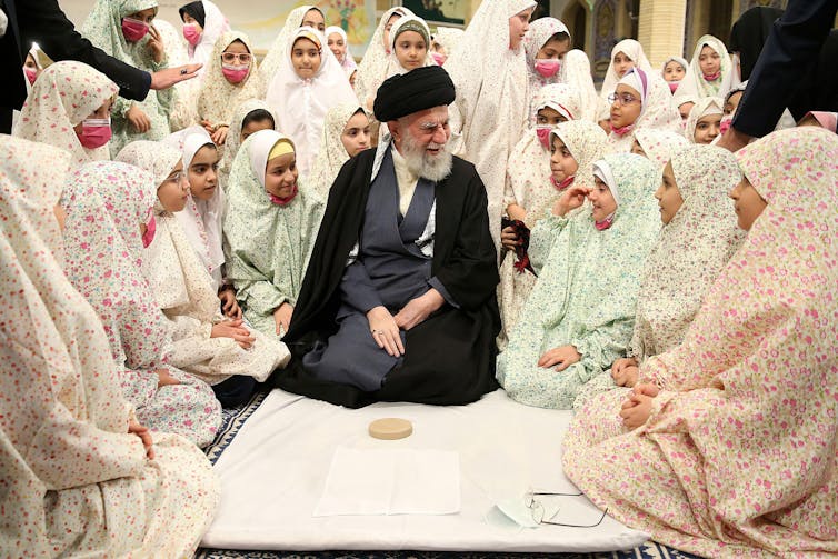 An elderly man in Islamic clerical clothes with Iranian schoolgirls in traditional costume.