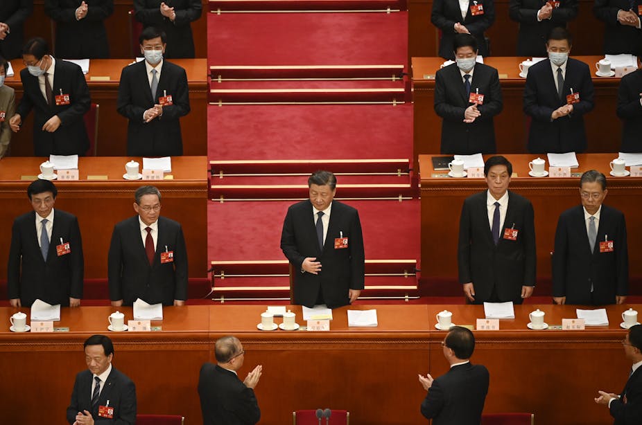 Xi Jinping debout entouré d'hommes qui l'applaudissent