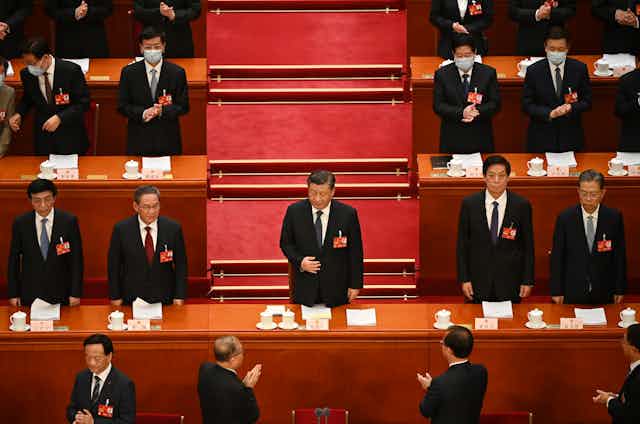 Xi Jinping debout entouré d'hommes qui l'applaudissent