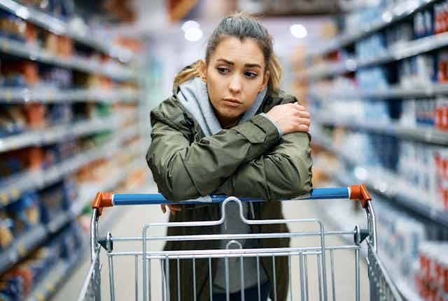 Young woman leaning on a grocery cart in a supermarket aisle looking worried
