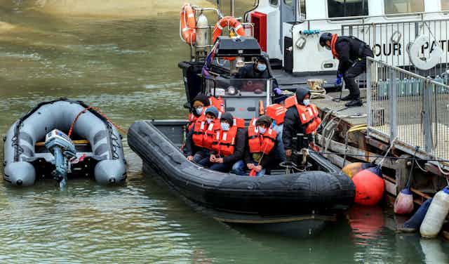 A small rubber boat of young men in red lifejackets arrives at a dock in Dover