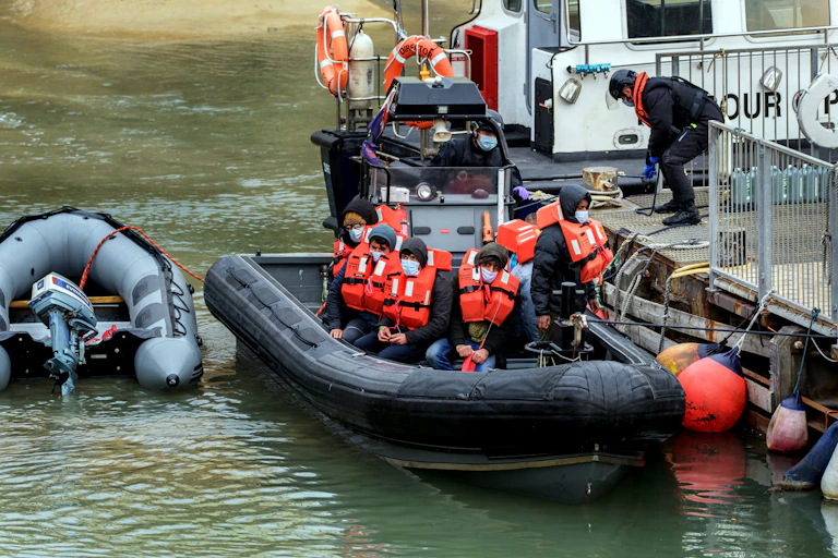 A small rubber boat of young men in red lifejackets arrives at a dock in Dover