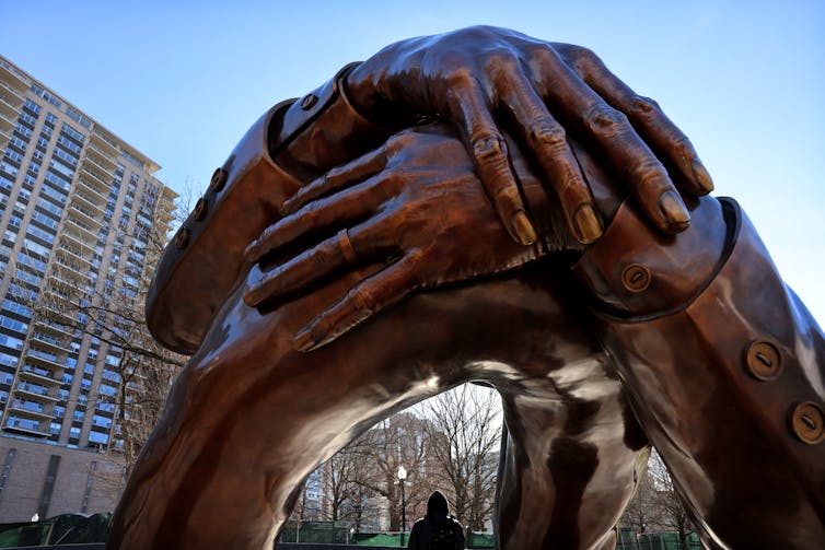 A statue of arms and hands has a space underneath where visitors can walk.