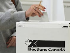 A woman's hand puts a ballot into a ballot box.