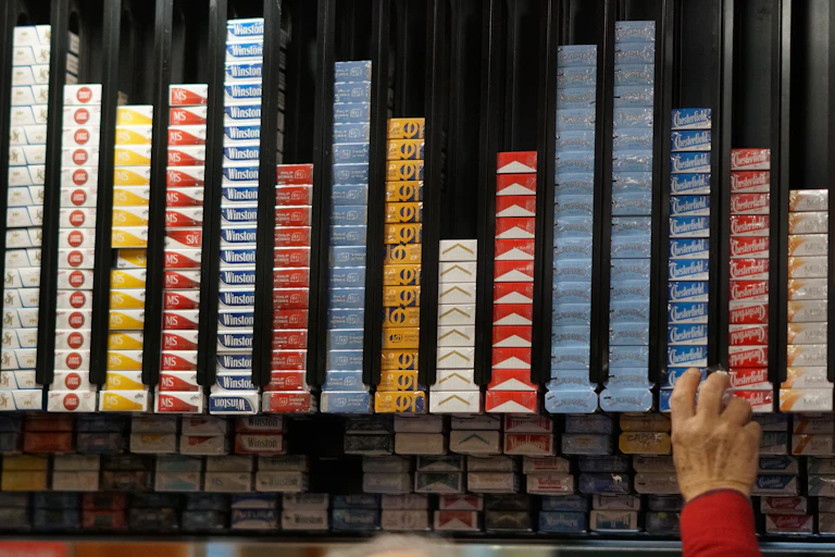 A person reaching for a pack of cigarettes from a shop shelf