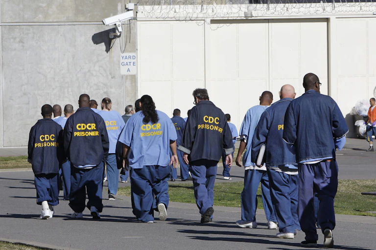 A group of mostly Black men walk away from the camera in blue prison uniforms.