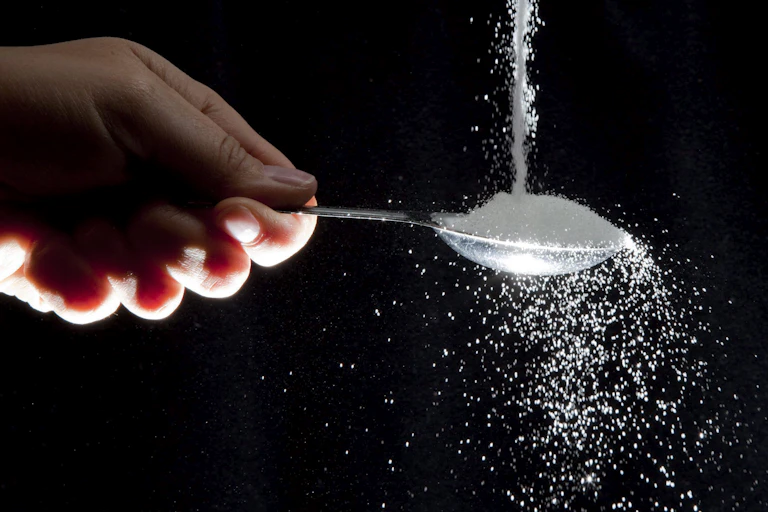 A hand holds a spoon as sugar pours onto it