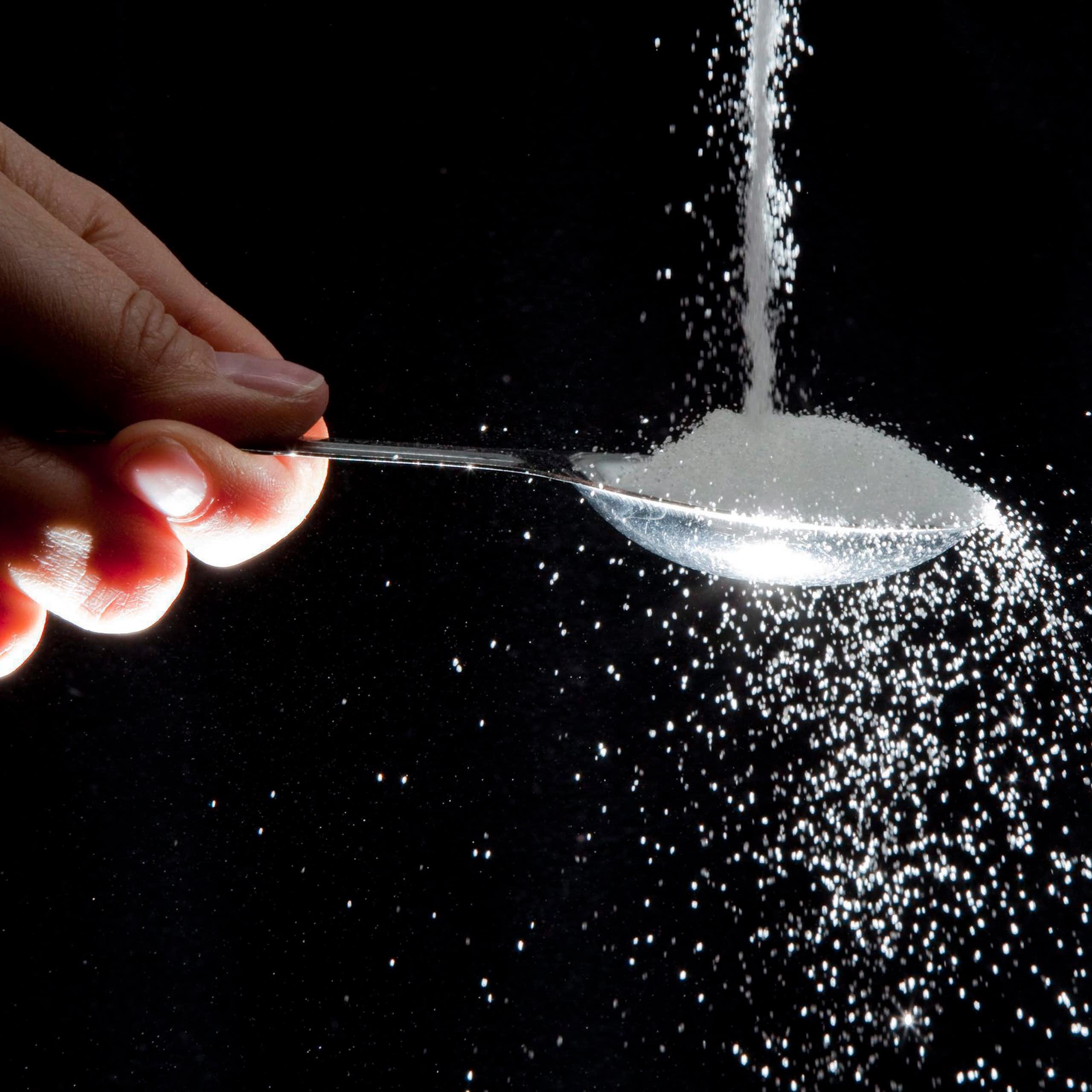 A hand holds a spoon as sugar pours onto it