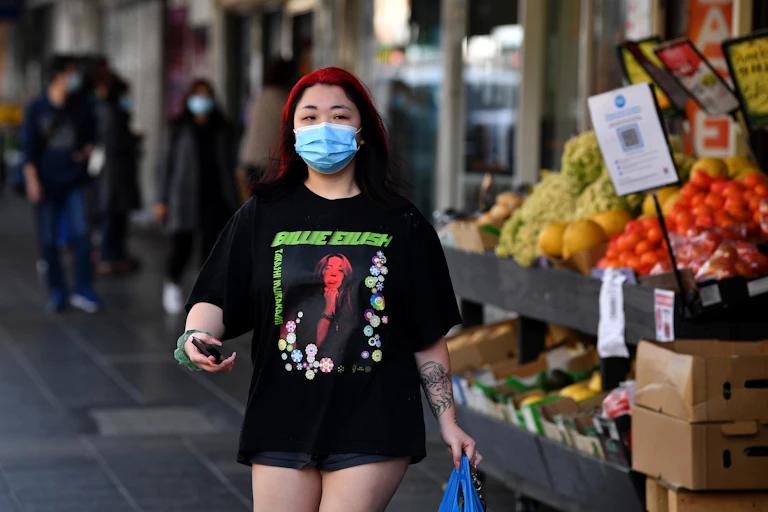 Young woman wearing mask holding phone and shopping bag outside grocery shop