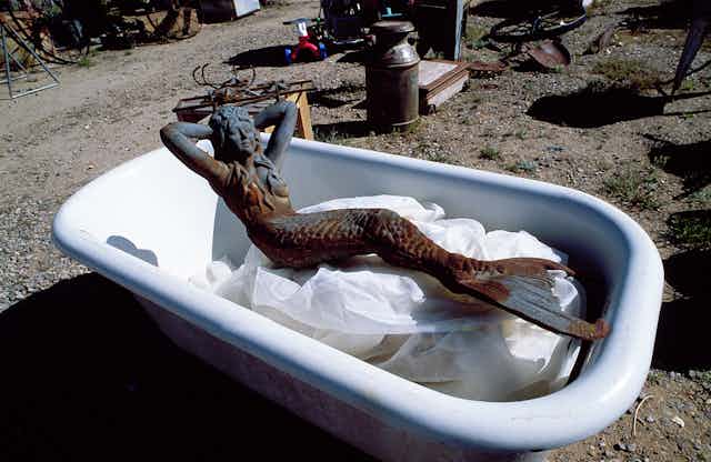 Escultura de metal de una sirena dentro de una bañera.