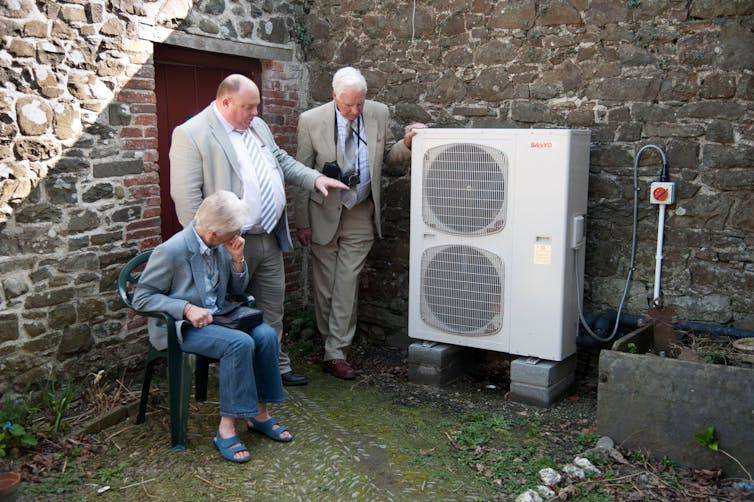 Três pessoas olhando para uma unidade de bomba de calor de fonte de ar.