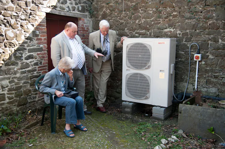 Three people looking at an air source heat pump unit.