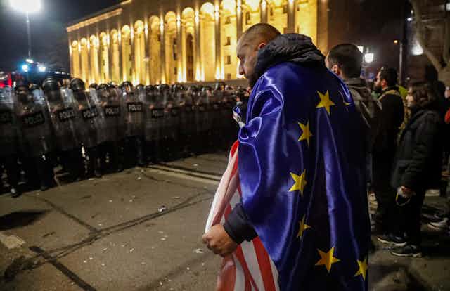 Protesters, one wearing an EU flag, stand opposite riot police in Tbilisi, Georgia, March 8 2023.