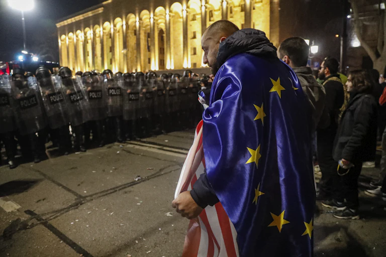 Protesters, one wearing an EU flag, stand opposite riot police in Tbilisi, Georgia, March 8 2023.