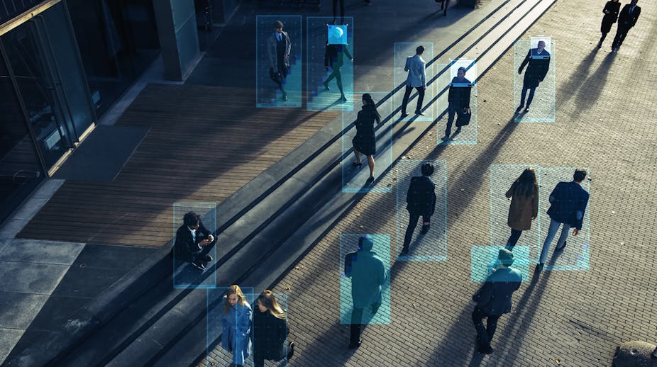 A number of human beings walk in different directions. The angle shows them from above and they are casting long shadows. Blue digital boxes frame each figure.