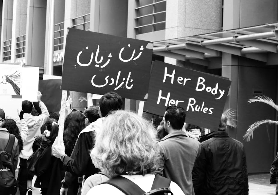 Men and women carrying banners in Farsi and English in support of women's rights in Iran.