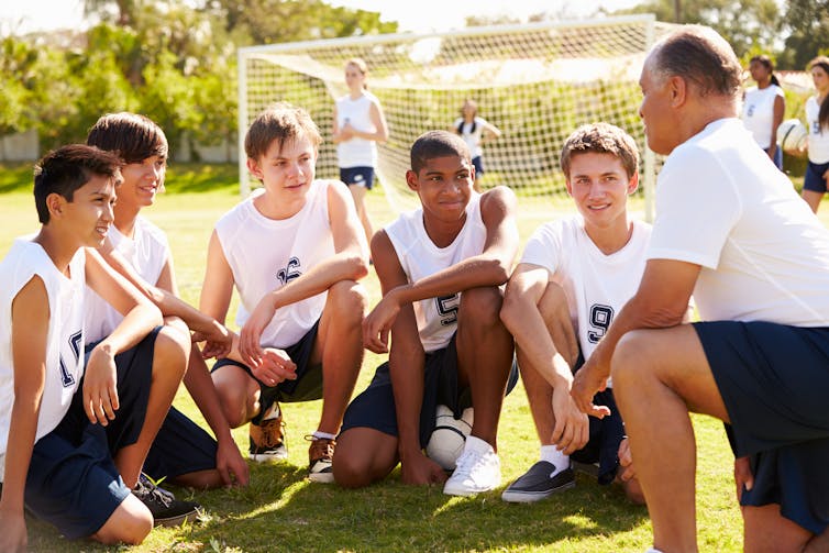 A group of boys on a soccer field, talking with their coach