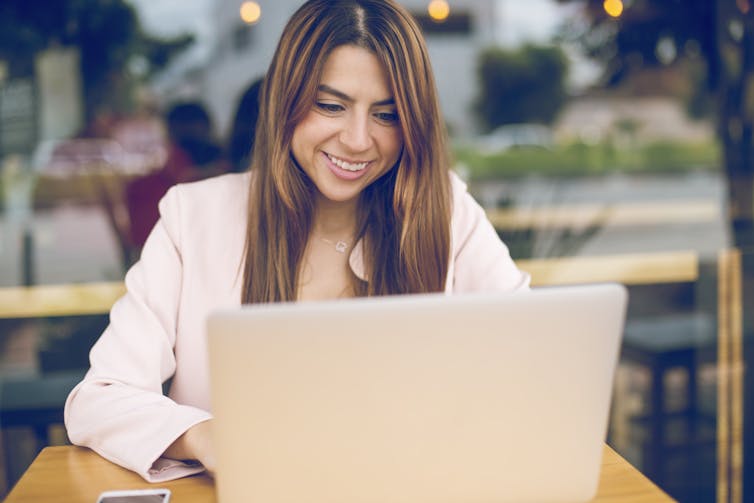 Young woman with long hair wearing white blazer smiles at laptop screen