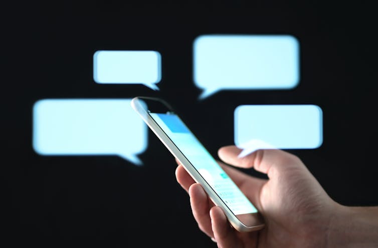A hand holding a smartphone with speech bubbles around it.