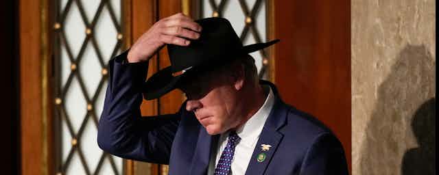 A man in a black cowboy hat in a blue suit and tie.