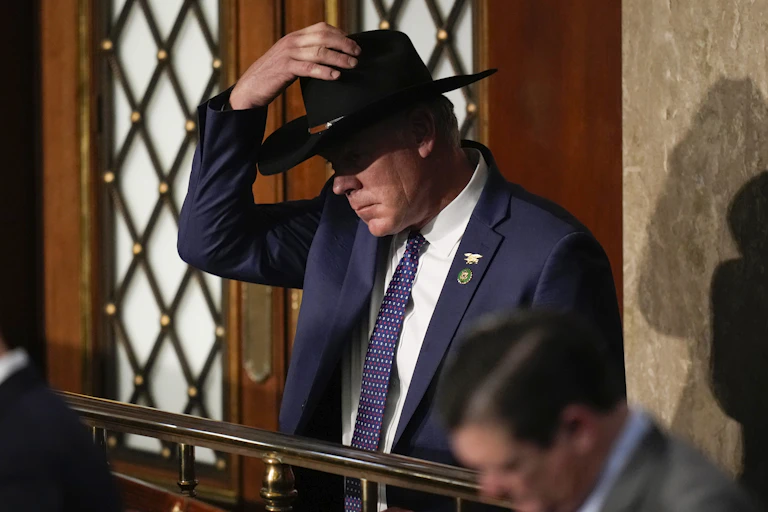 A man in a black cowboy hat in a blue suit and tie.