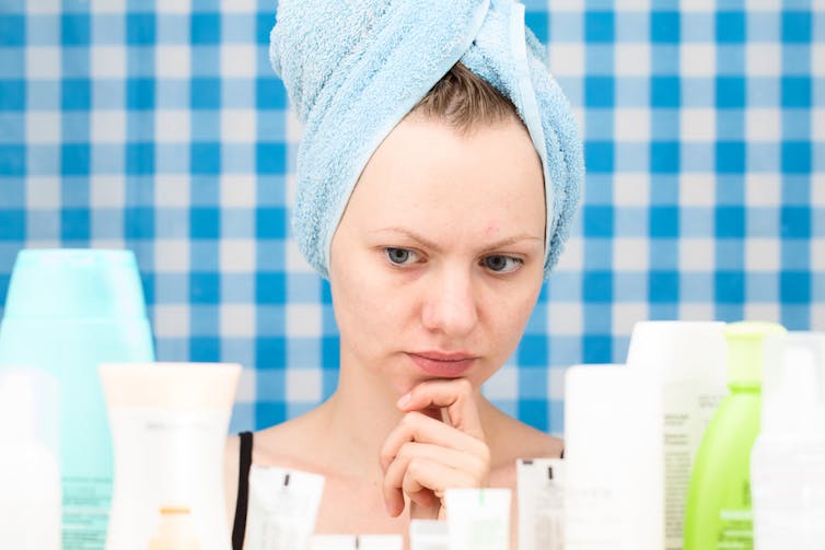 A woman looks critically at skincare and shampoo bottles.