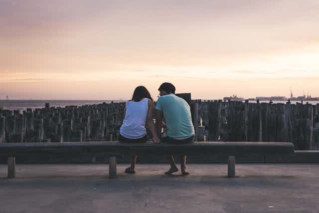 young man and woman sit by beach talking at sunset