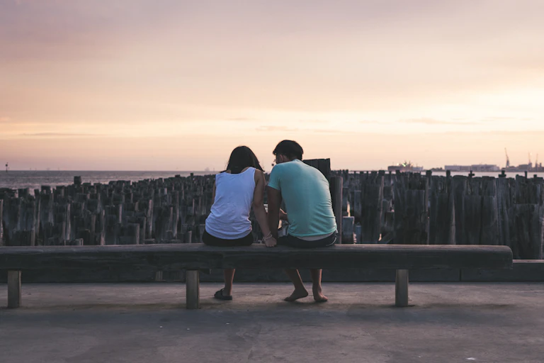 young man and woman sit by beach talking at sunset