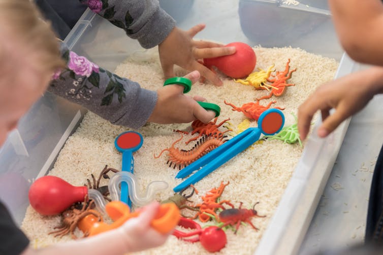 children's hands dig through sand for plastic toys
