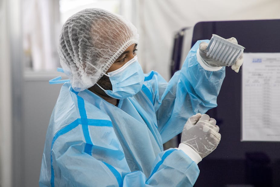 Person wearing protective cap, mask, gown and gloves holds a piece of laboratory equipment