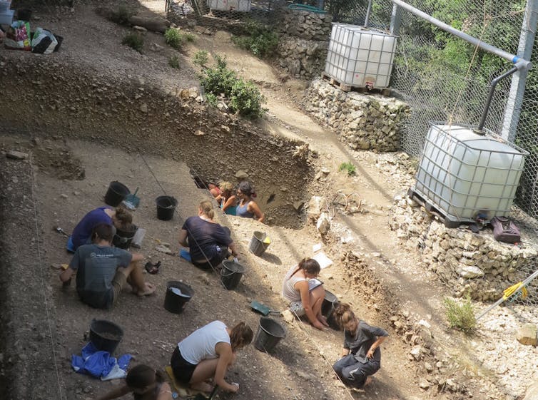 People kneeling on dirt ground, excavating.