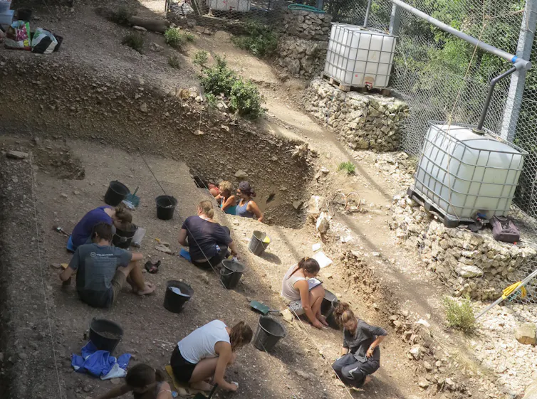 People kneeling on dirt ground, excavating.