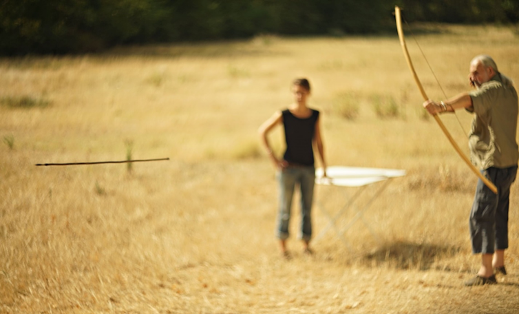 Arrow flies while man holds bow and woman observes