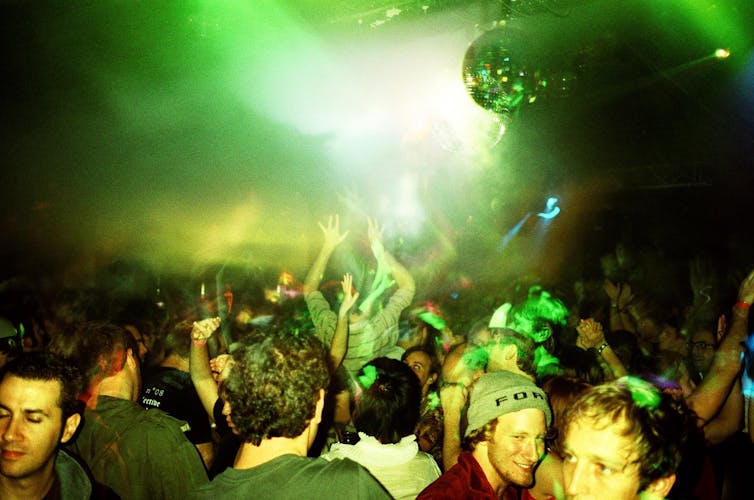 a group of people dance in a green-lit venue, with a disco ball hanging from the ceiling