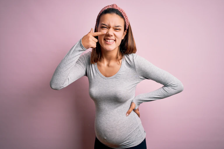A pregnant woman points at her nose, smiling.