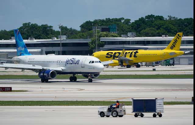 A white airplane withJetBlue written on it passes a yellow one with Spirit written on it.
