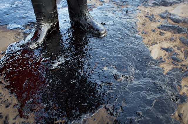 A person's boots, standing in an oil spill.