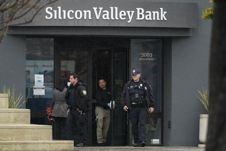 άνδρες με στολή βγαίνουν από ένα κτίριο με γυάλινες πόρτες κάτω από μια πινακίδα που γράφει silicon Valley bank