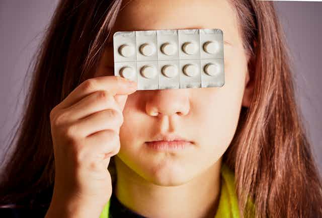 Une adolescente tient une plaquette de médicaments devant ses yeux.