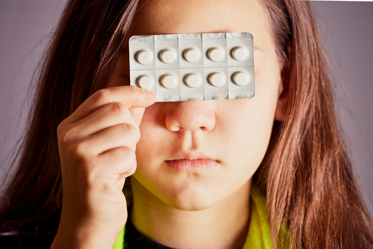 Une adolescente tient une plaquette de médicaments devant ses yeux.