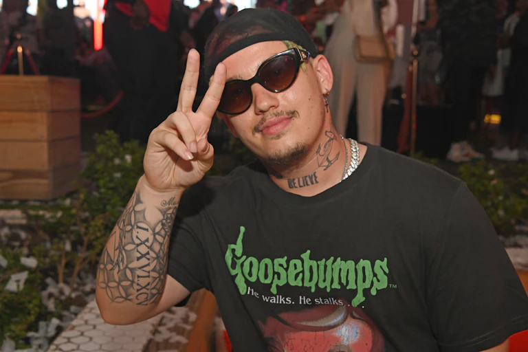 A man holds up his finger in a 'v' sign for victory. He's wearing sunglasses and smiling.
