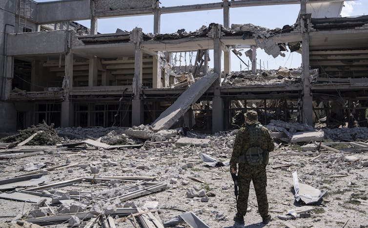 A soldier is seen looking at ruins of a building.