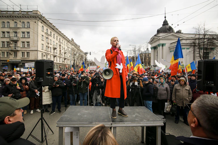 A woman with a loudhailer stands on a platform addressing a crowd waving Moldovan flags.