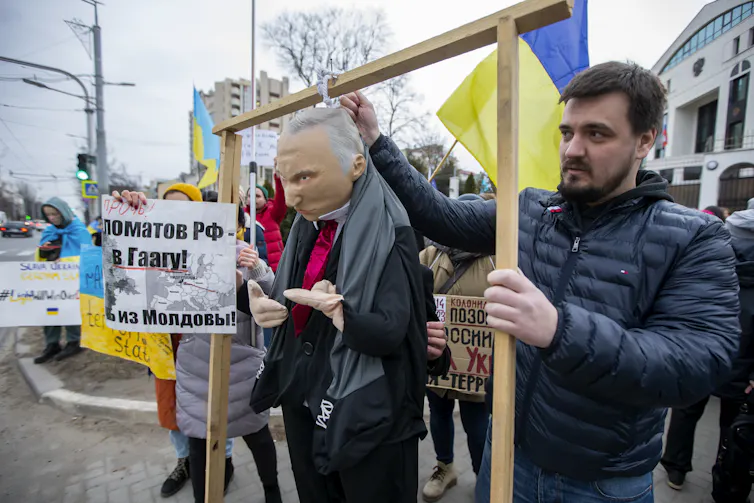 A man holds up a dummy of Russian president Vladimir Putin against a backdrop of Ukrainian and Moldovan flags.