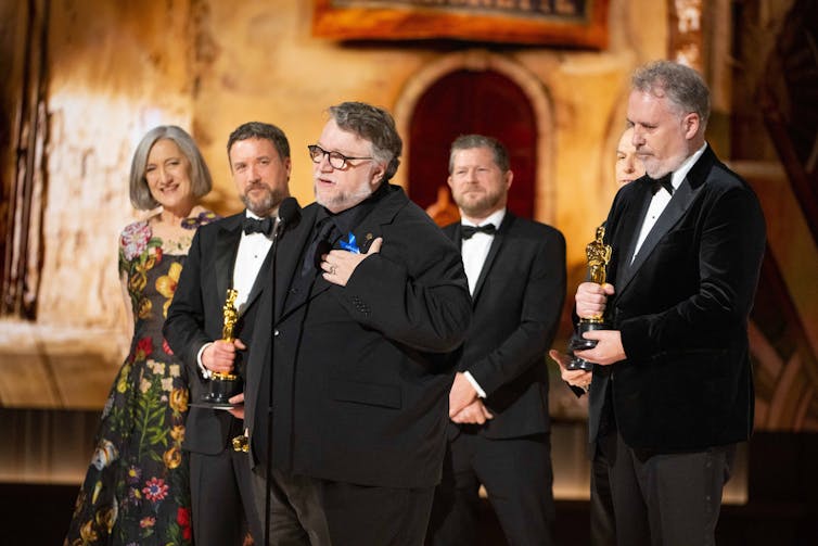 Guillermo del Toro, Mark Gustafson, Gary Ungar and Alex Bulkley on stage at the Oscars speaking into a microphone.