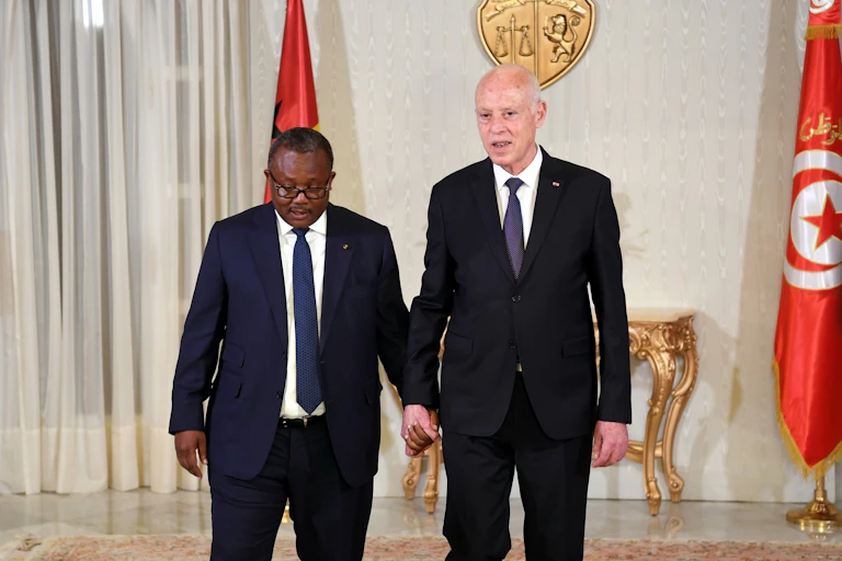 Two men in suits and ties pose for pictures holding hands.