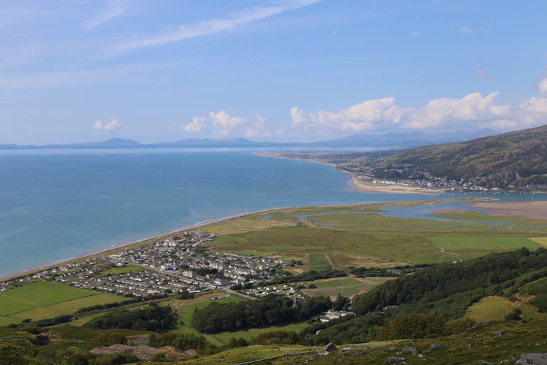 A view of a small village from above. It lies right next to the sea. There is a large, sandy estuary to the right of the village and a range of mountains in the distance.