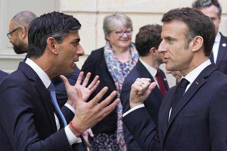 Rishi Sunak holding out his hands and Emmanuel Macron making a fist as they chat.