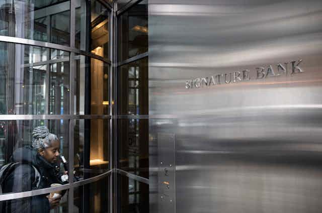 A black woman enters a glass door next to a steel wall with words signature bank on it